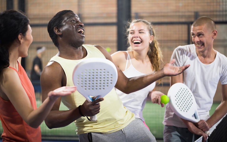 Group of cheerful paddle tennis players talking on closed court